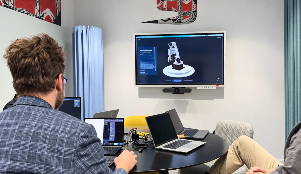 El equipo de Cloudly revisa un modelo de brazo robótico en el visor 3D de productos, en la pantalla de una sala de reuniones.
