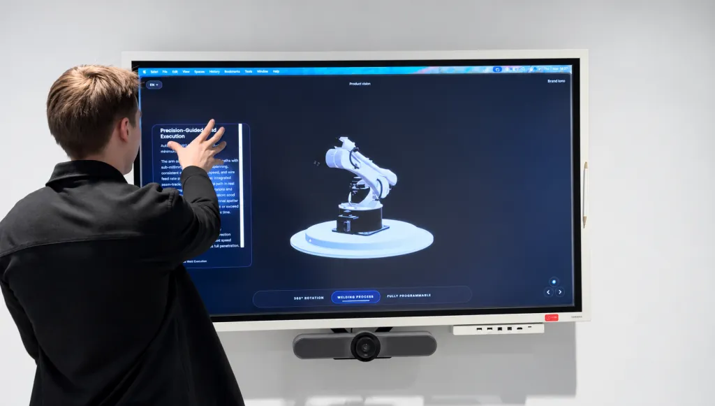 Un miembro del equipo maneja el visor 3D interactivo de productos de Cloudly en una pantalla táctil mural, que muestra un brazo robótico industrial.